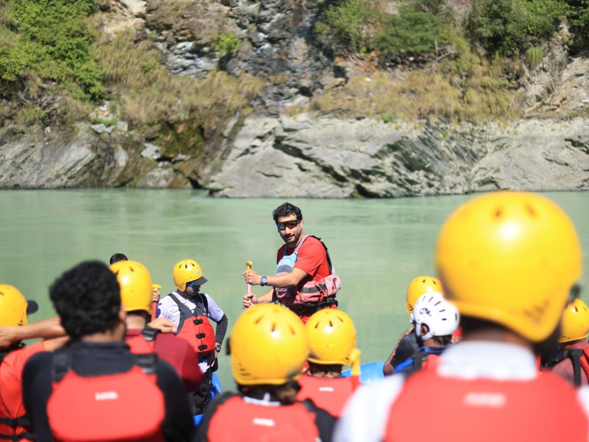IRF-certified guide giving a safety briefing to helmeted rafters on the Ganga riverbank