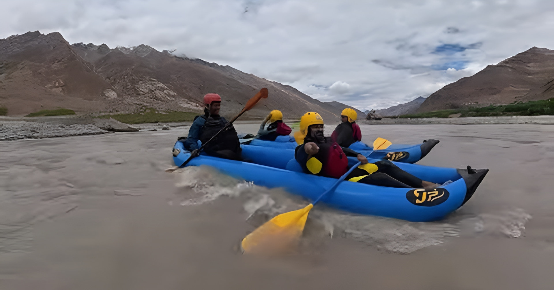 Rafters paddling inflatable kayaks down a Himalayan river beneath cloudy mountain skies