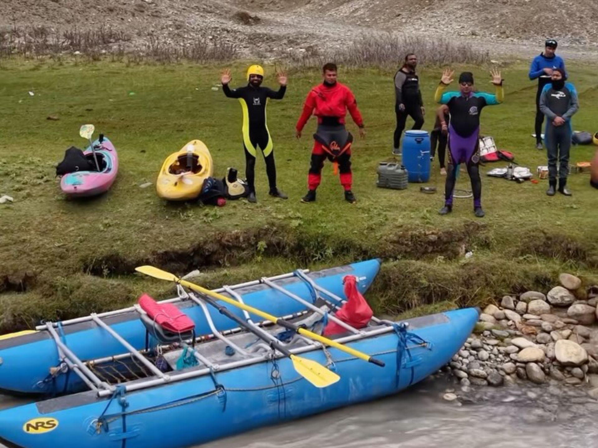 Guides in river gear beside kayaks and a blue expedition raft on the riverbank