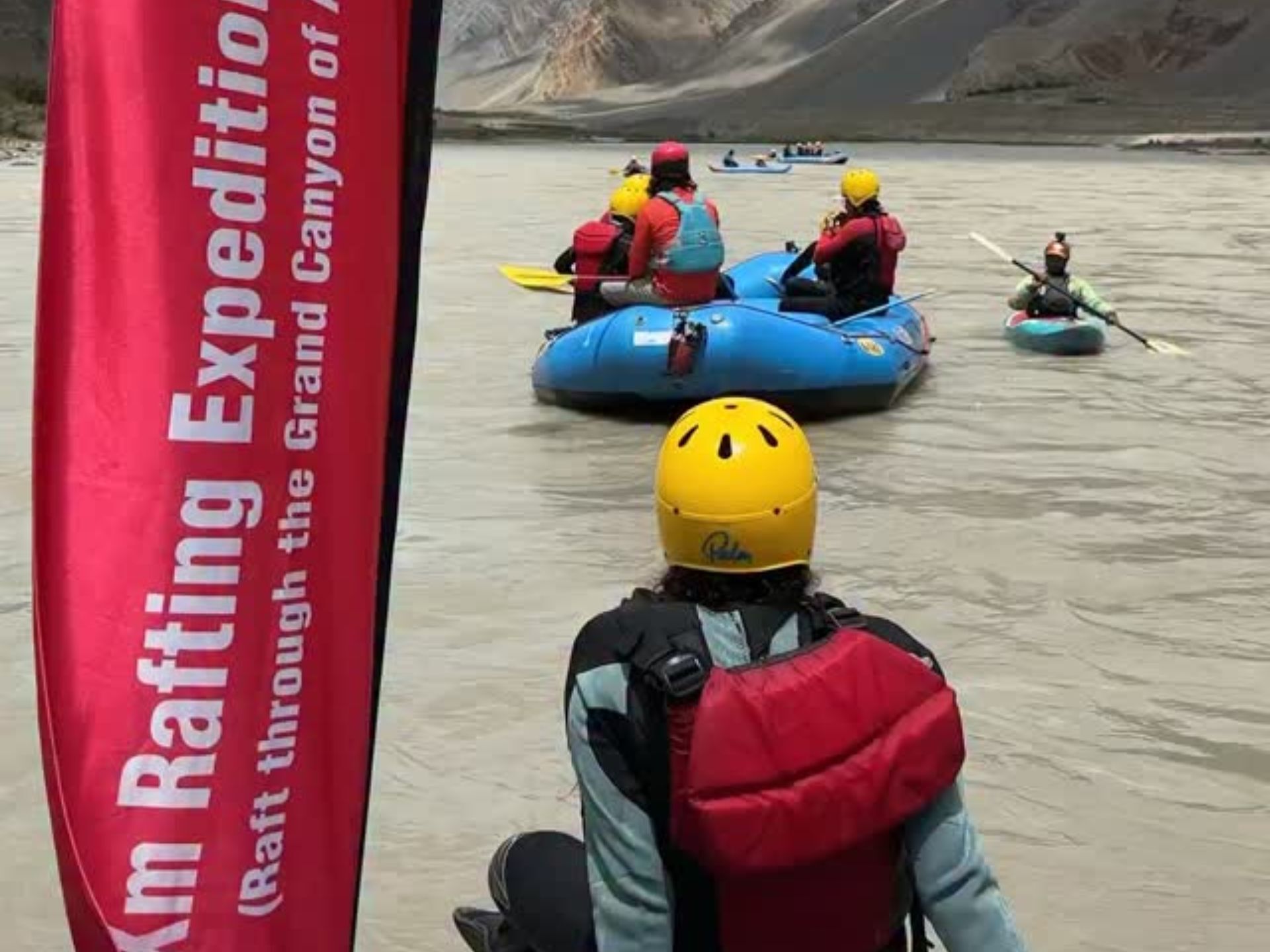 Rafters wearing helmets and life jackets with a safety kayaker on the river