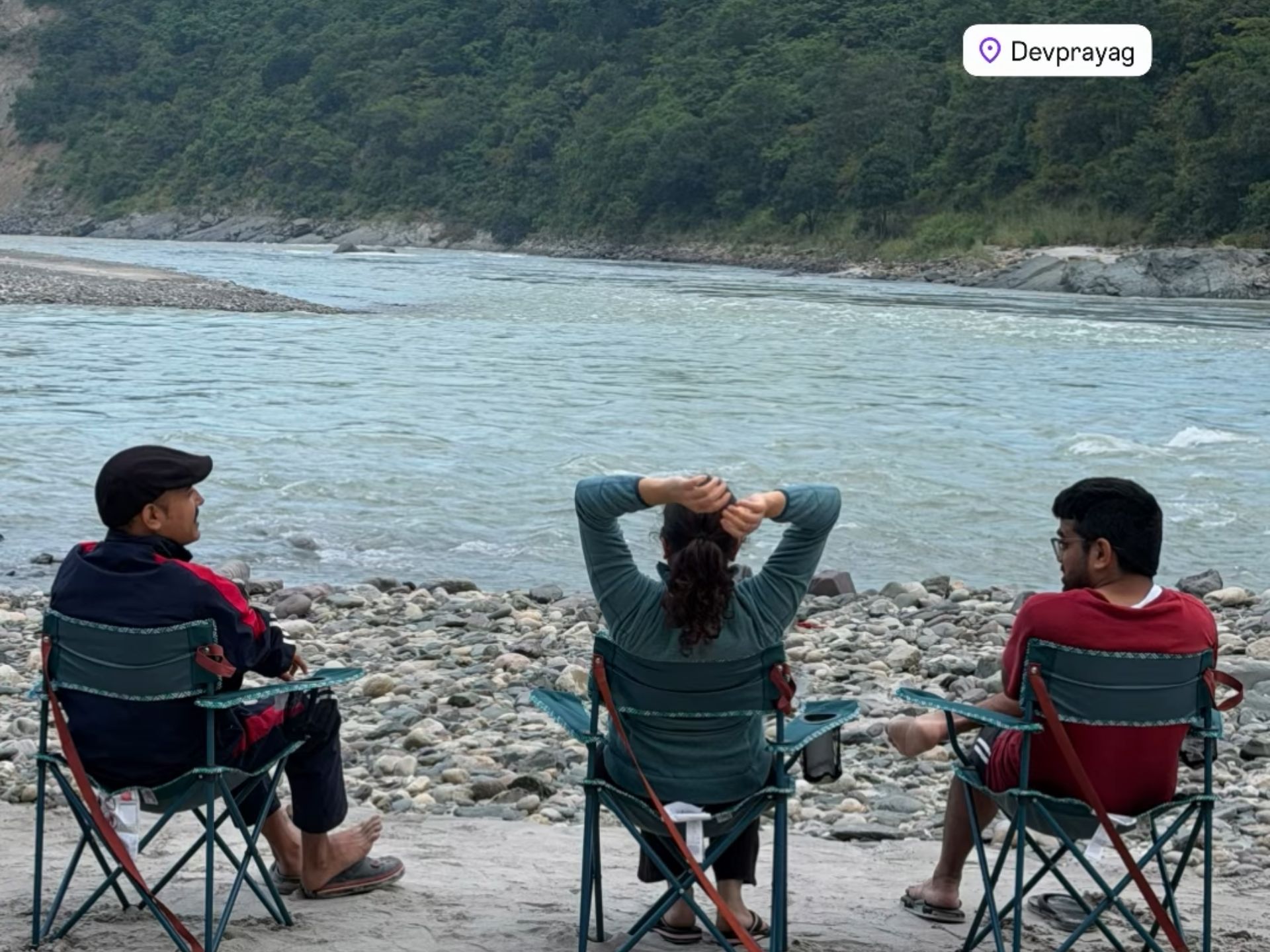 Guests relaxing in camping chairs beside the river at Devprayag