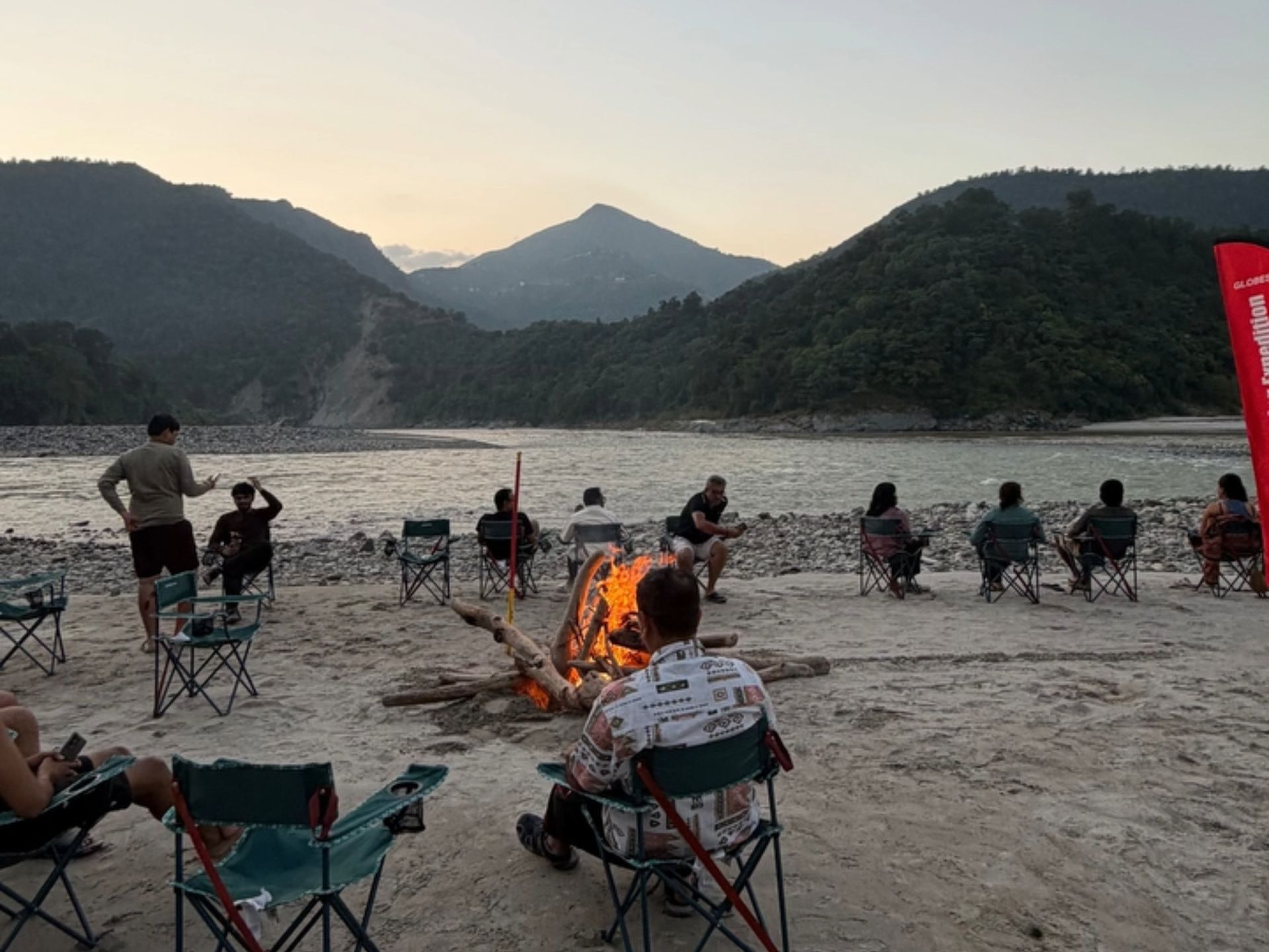 An evening bonfire with guests gathered at a riverside camp