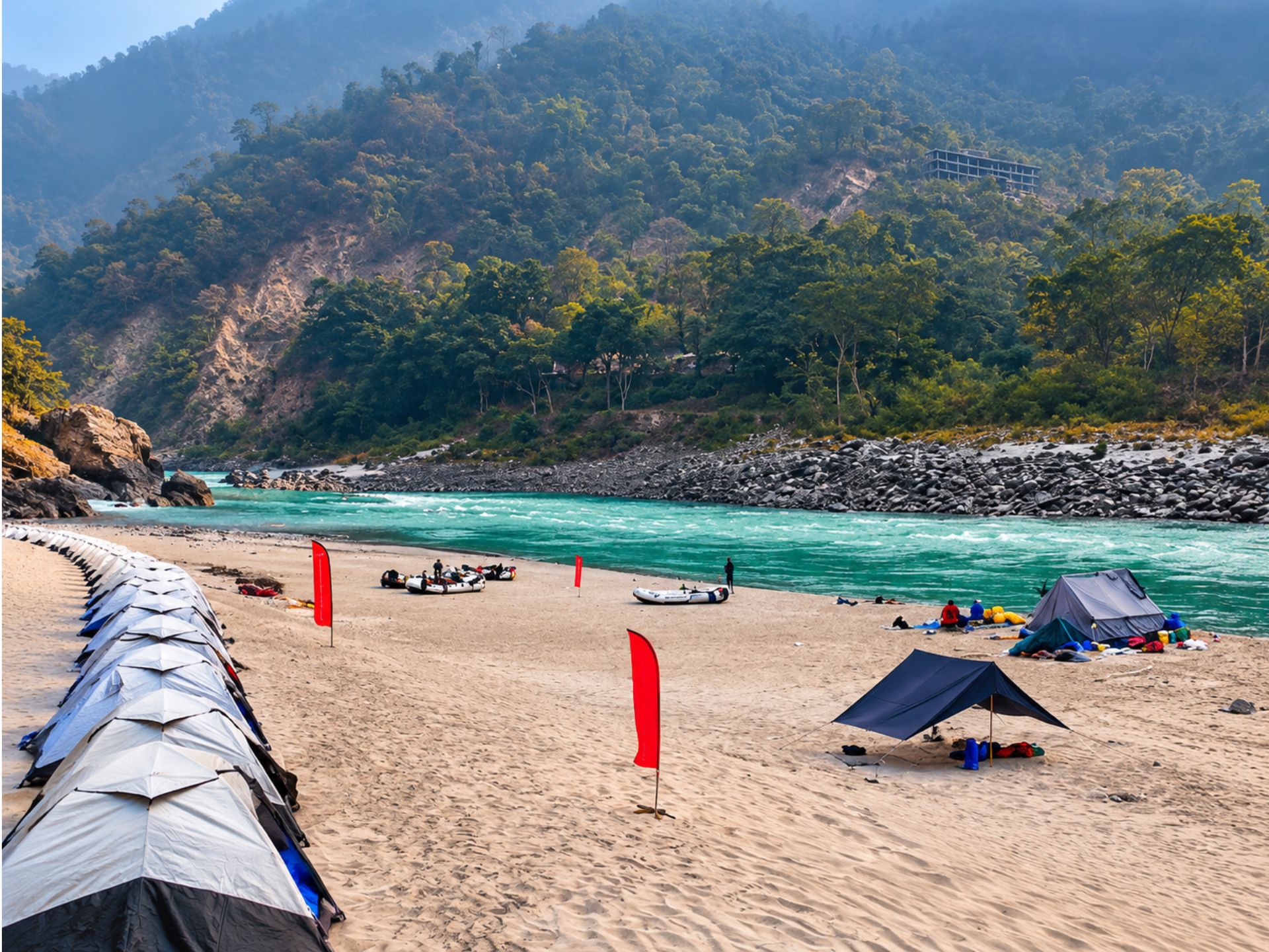 Riverside tents on a sandy beach beside the turquoise river and forested hills